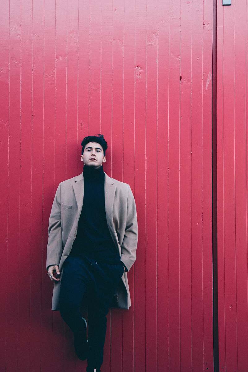 person man wearing coat leaning on red wall people