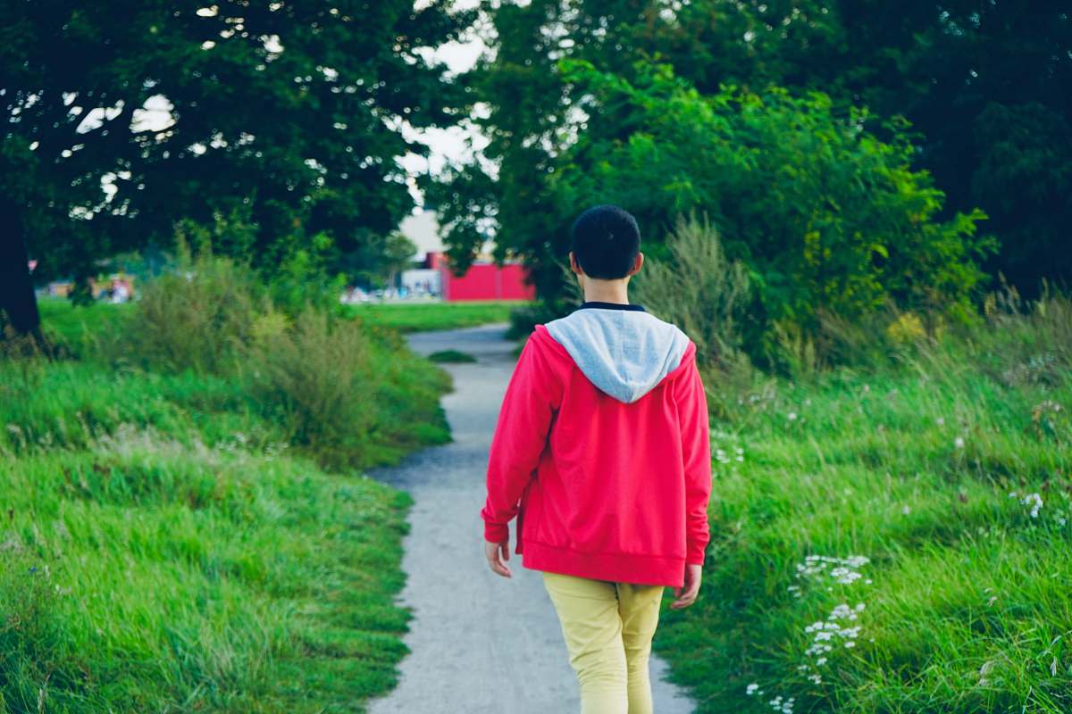apparel person walking on pathway near grasses clothing