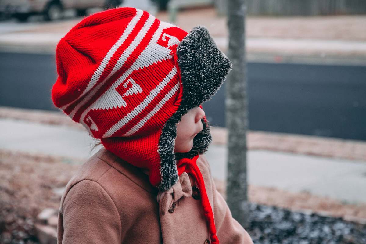 people toddler wearing red and white knit hat near road during daytime hat