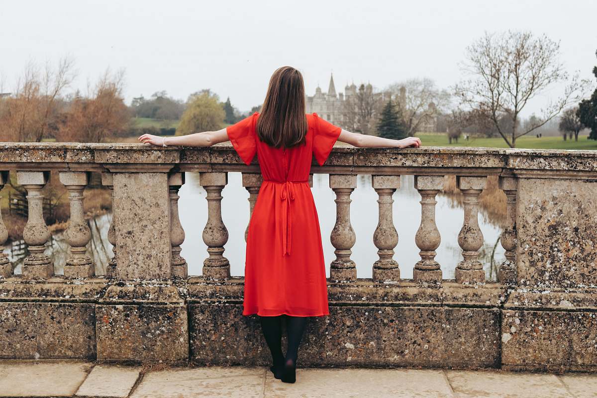 clothing woman in red dress looking at body of water and trees during daytime apparel