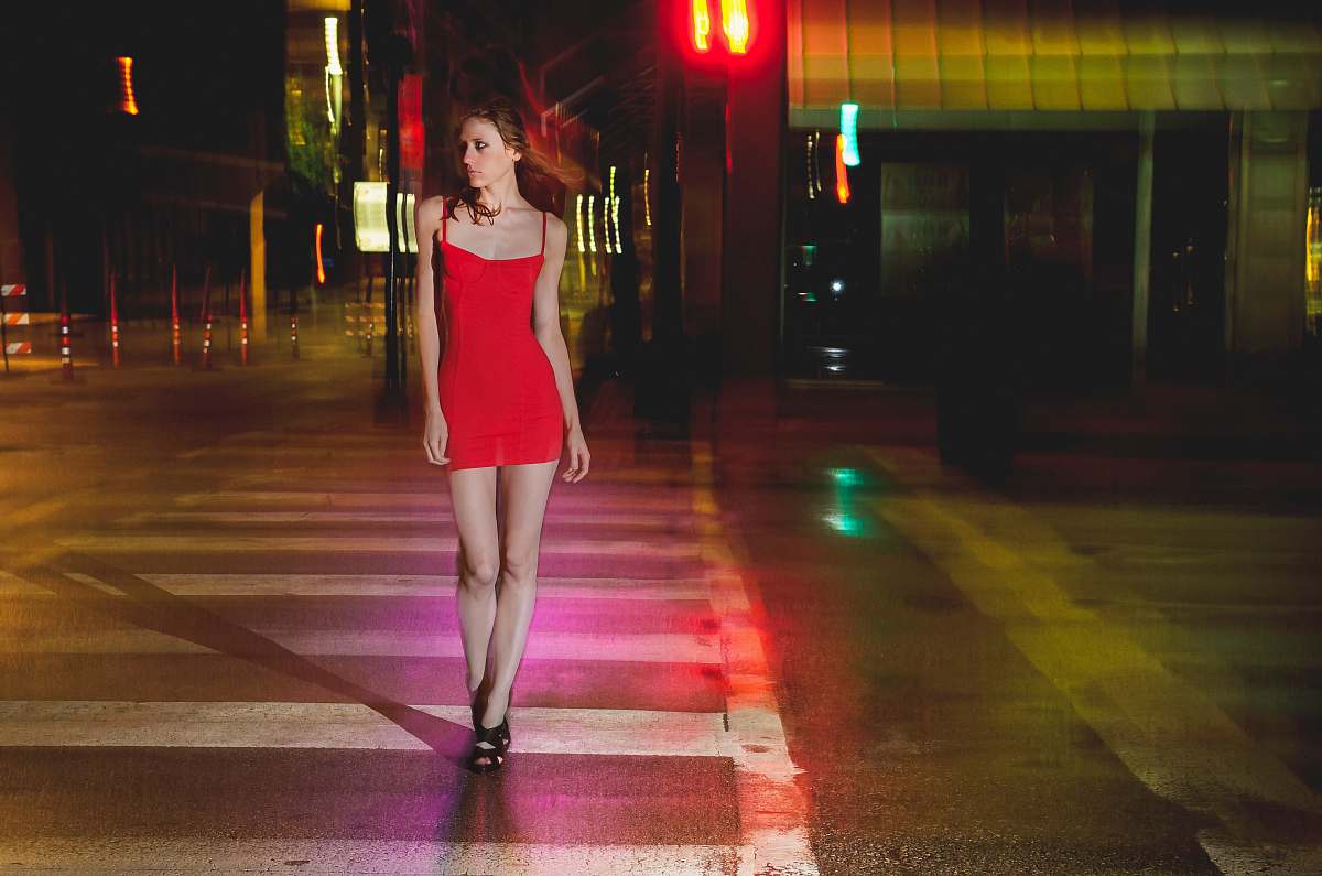 person woman in red spaghetti strap midi dress walking on pedestrian lane during nighttime city