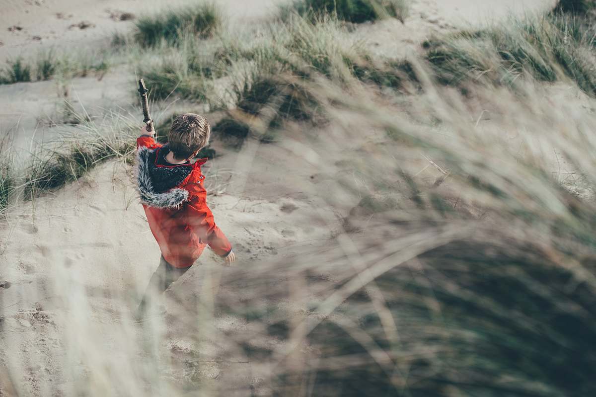 boy selective focus photo of person walking on gray sand with green grasses child