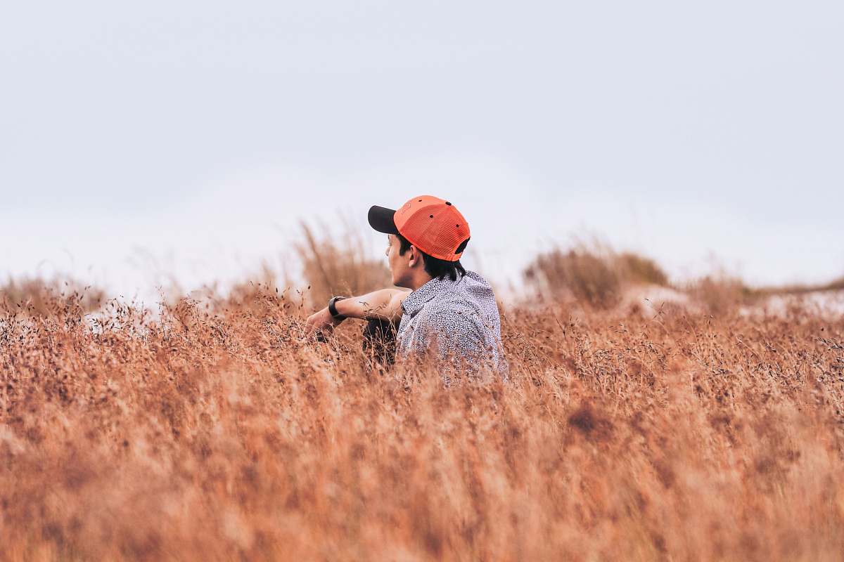 male sitting man wearing red cap on brown flower field at daytime cap