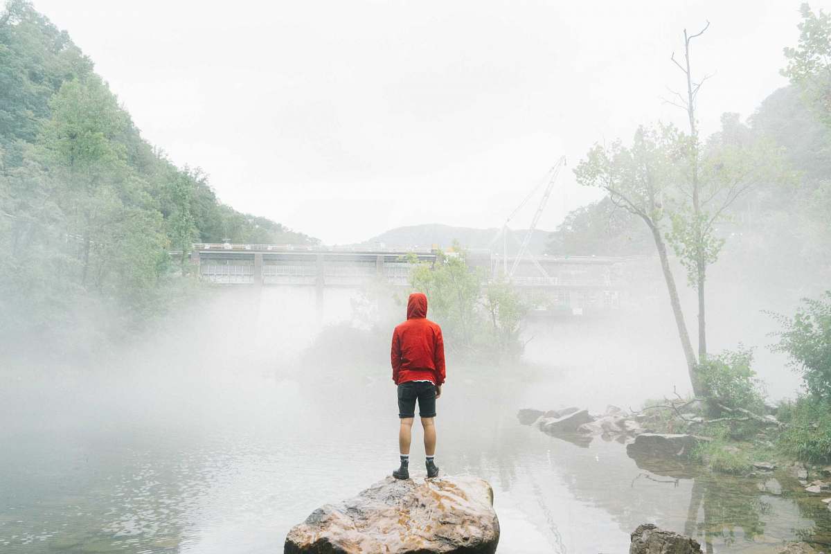 standing man standing on rock facing foggy creek lake