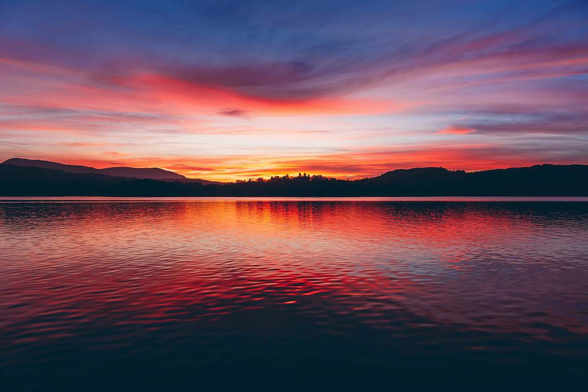 sunset silhouette photo of body of water and mountain sky