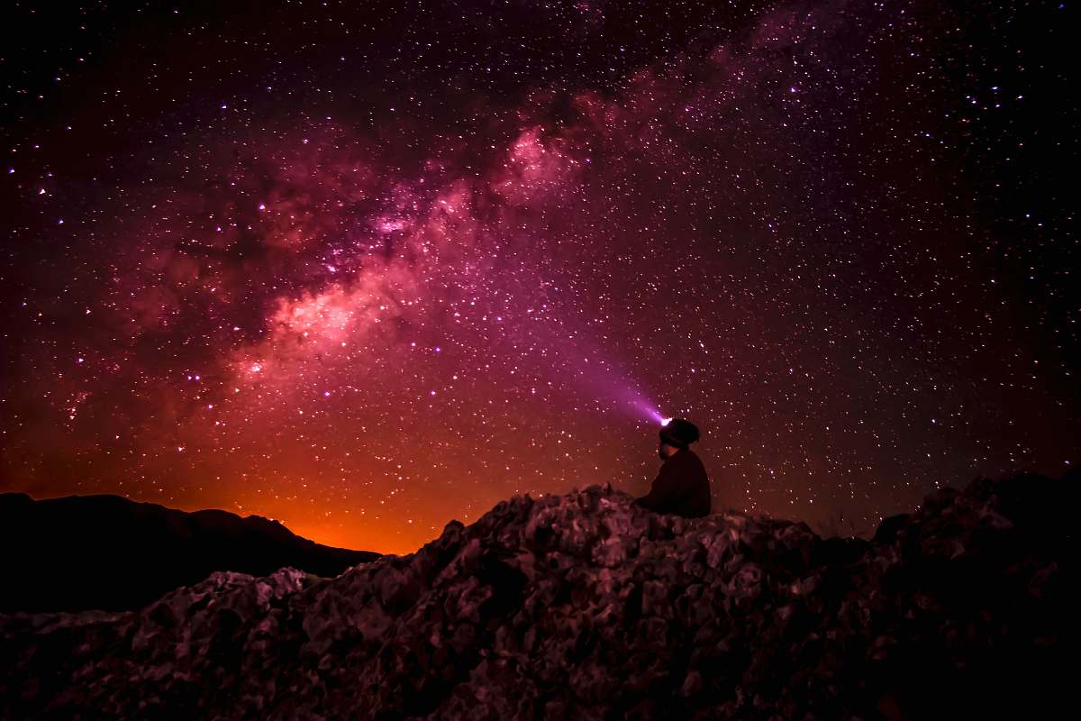 star silhouette photo of person holding flashlight under milk way stars