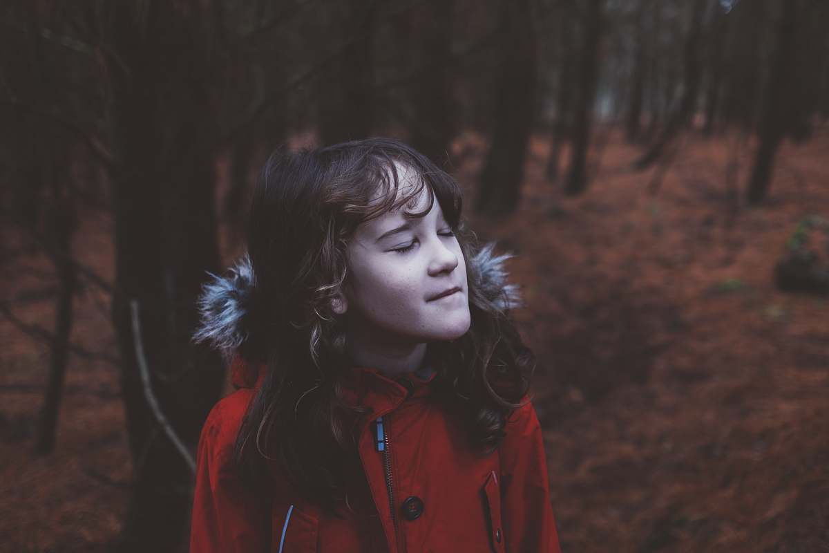 person girl wearing red coat standing near trees girl