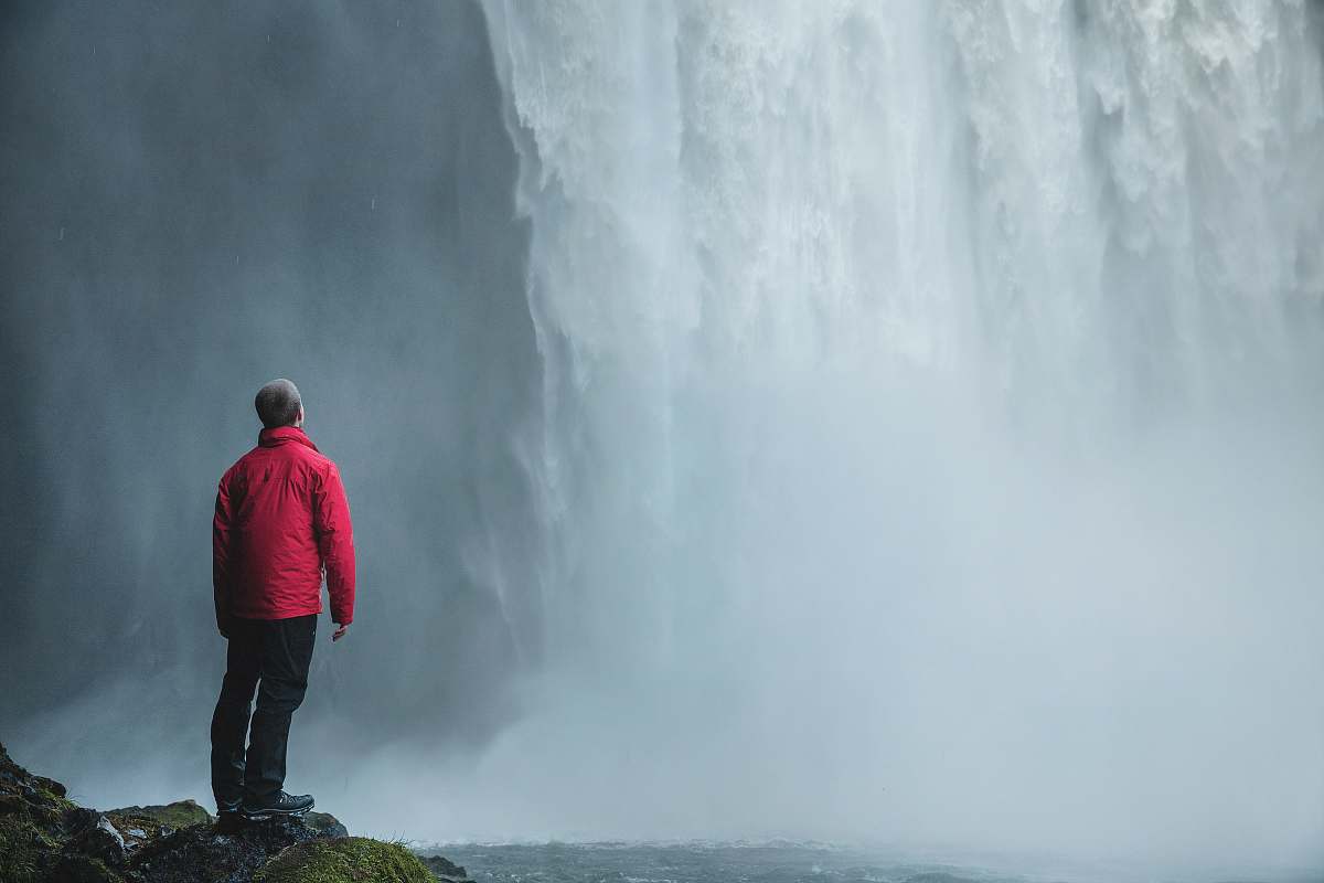 person man standing on a rock facing waterfalls human