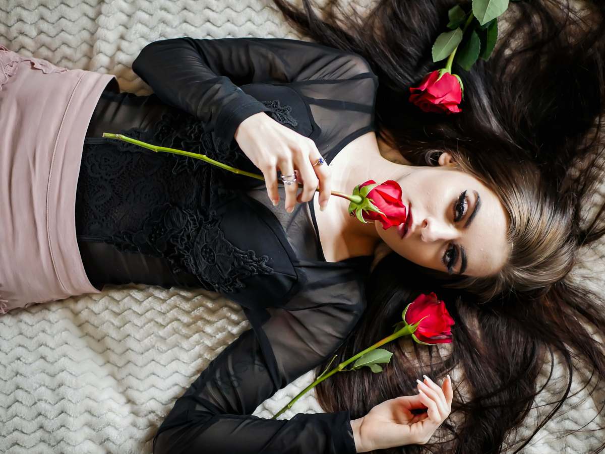 human woman lying on white bed holding red rose rose