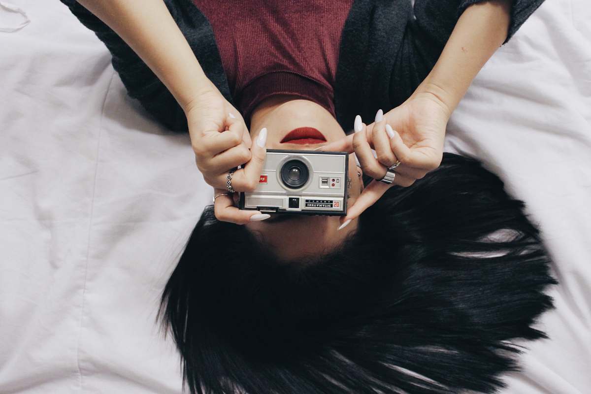camera lying woman in red and black top holding silver point and shoot camera human