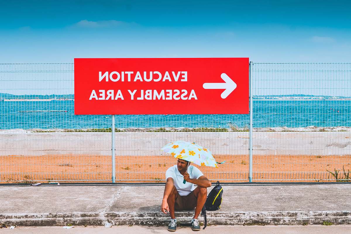 human man sitting beside the road while holding an umbrella umbrella