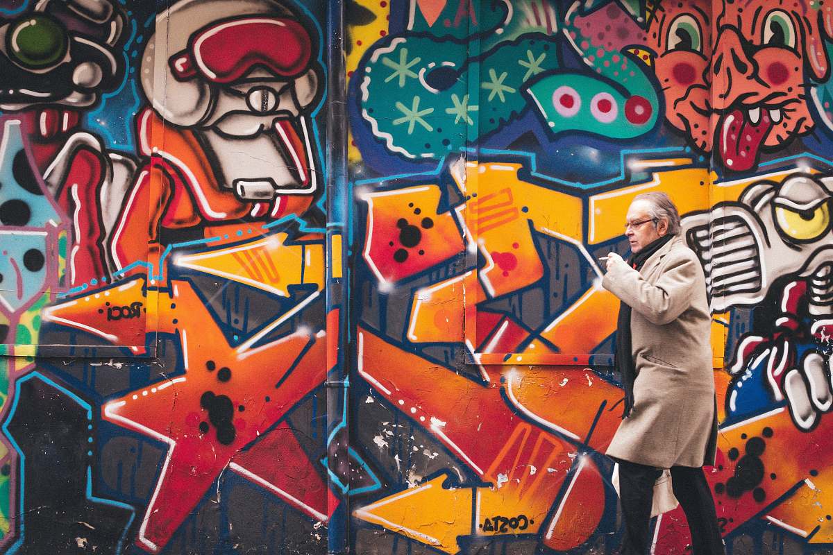graffiti man wearing grey coat walking beside wall with graffiti human