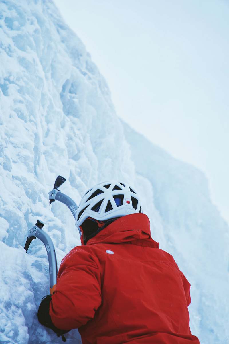 snow person in red jacket while climbing ice wall at daytime ice