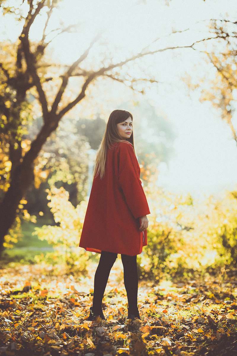 human selective focus photography of woman standing at dried-leaf filled ground under ray of sun people