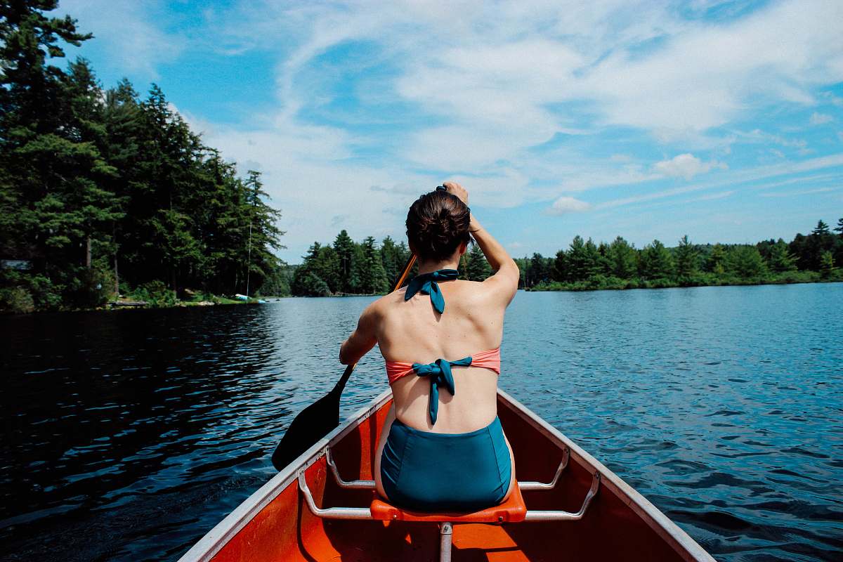 boat woman riding on boat while paddling under blue sky during daytime canoe