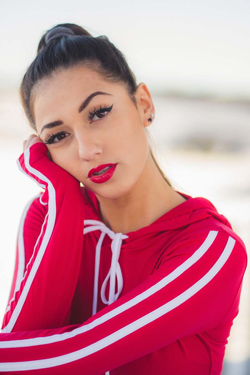 human woman wearing red and white pullover hoodie putting left hand on her face face