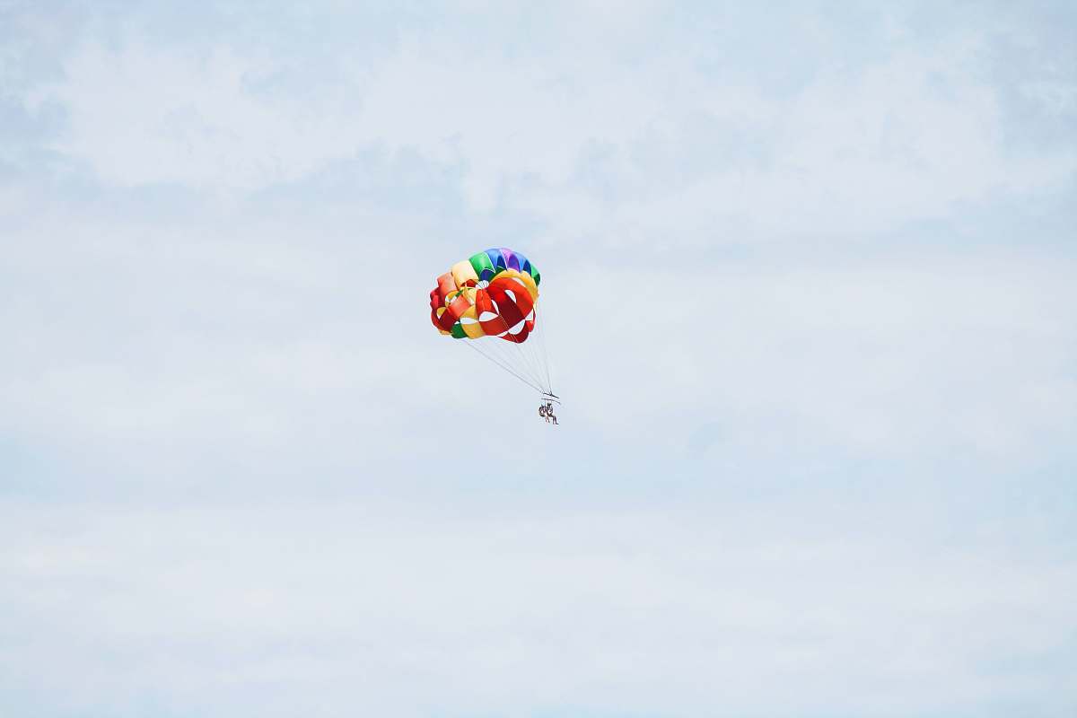 brown person on parachute sky diving under cumulus clouds pink
