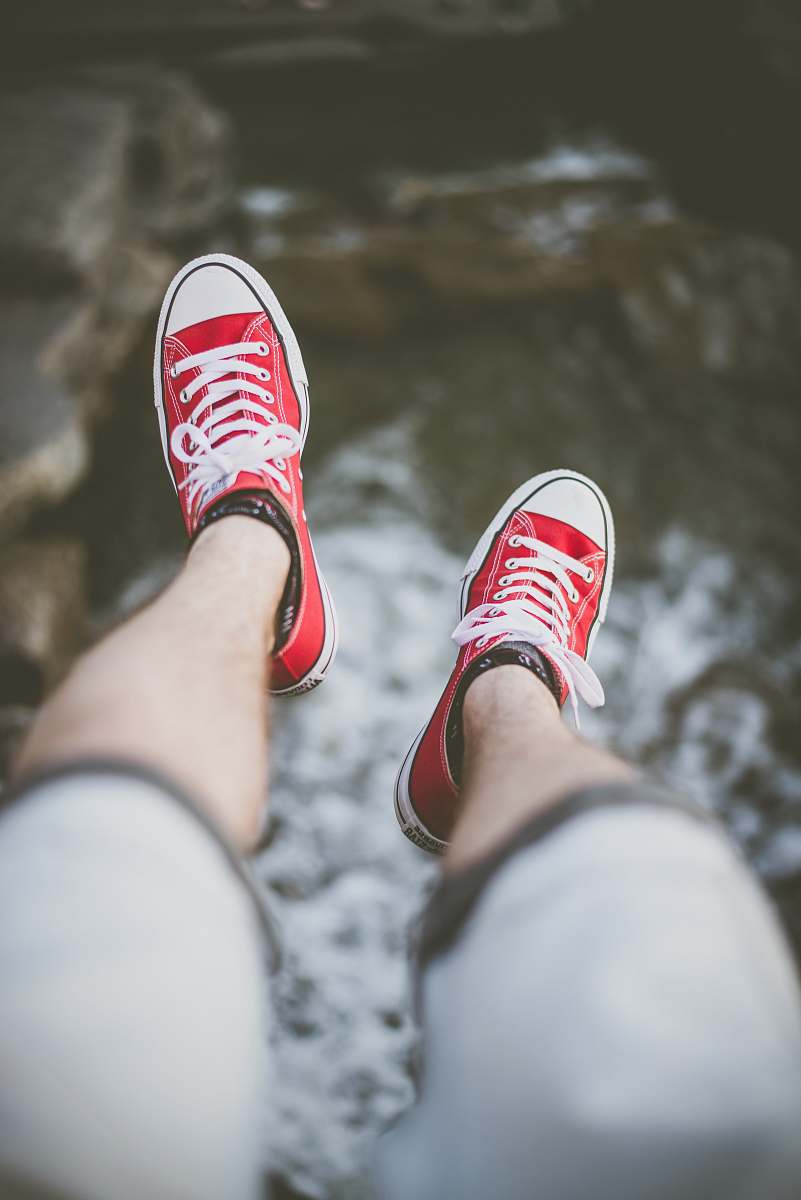 shoes selective focus photography of person wearing red low-top sneakers over body of water water