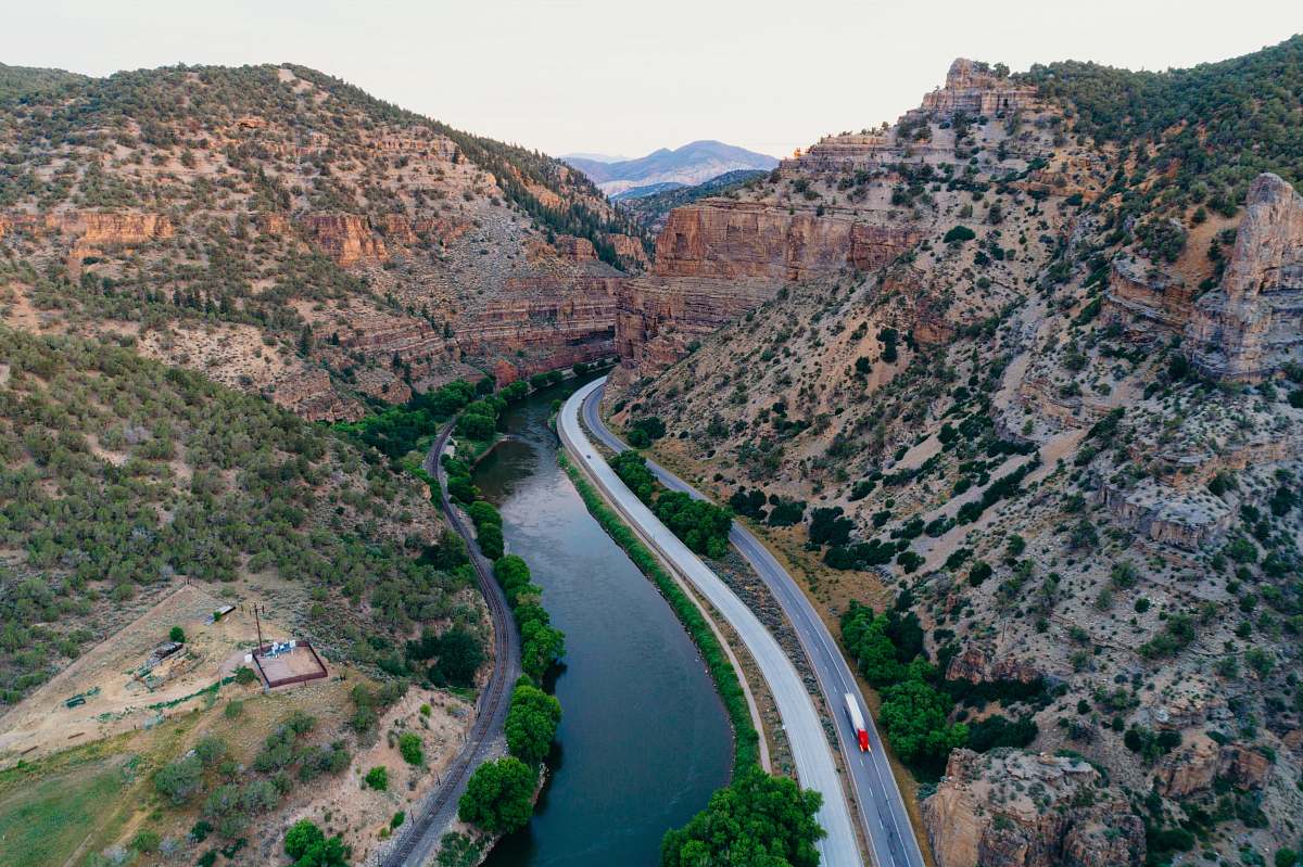 mountain aerial photo of road between river and mountain during daytime valley