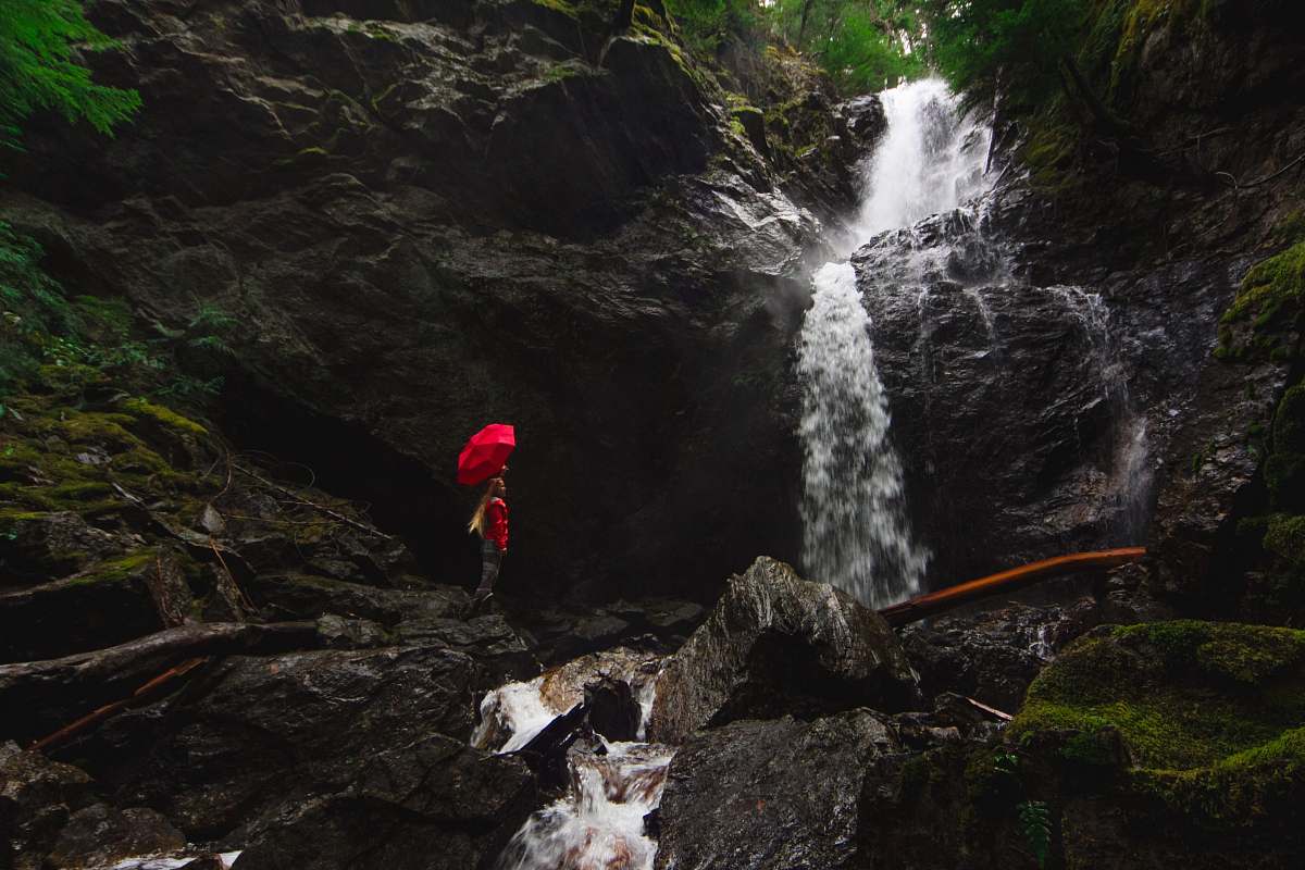 moss person standing on rock formation under red umbrella beside waterfalls waterfall