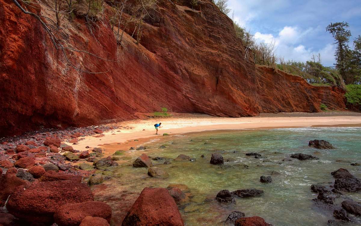 water person on seashore beside cliff during daytime rock