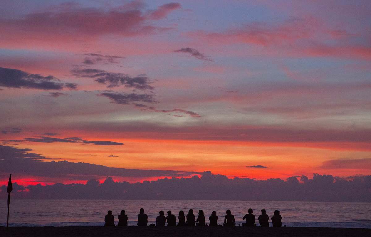people people sitting on seashore while watching golden hour sunrise