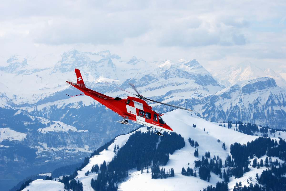 snow photo of flight of red and white rescue helicopter during snow daytime glacier