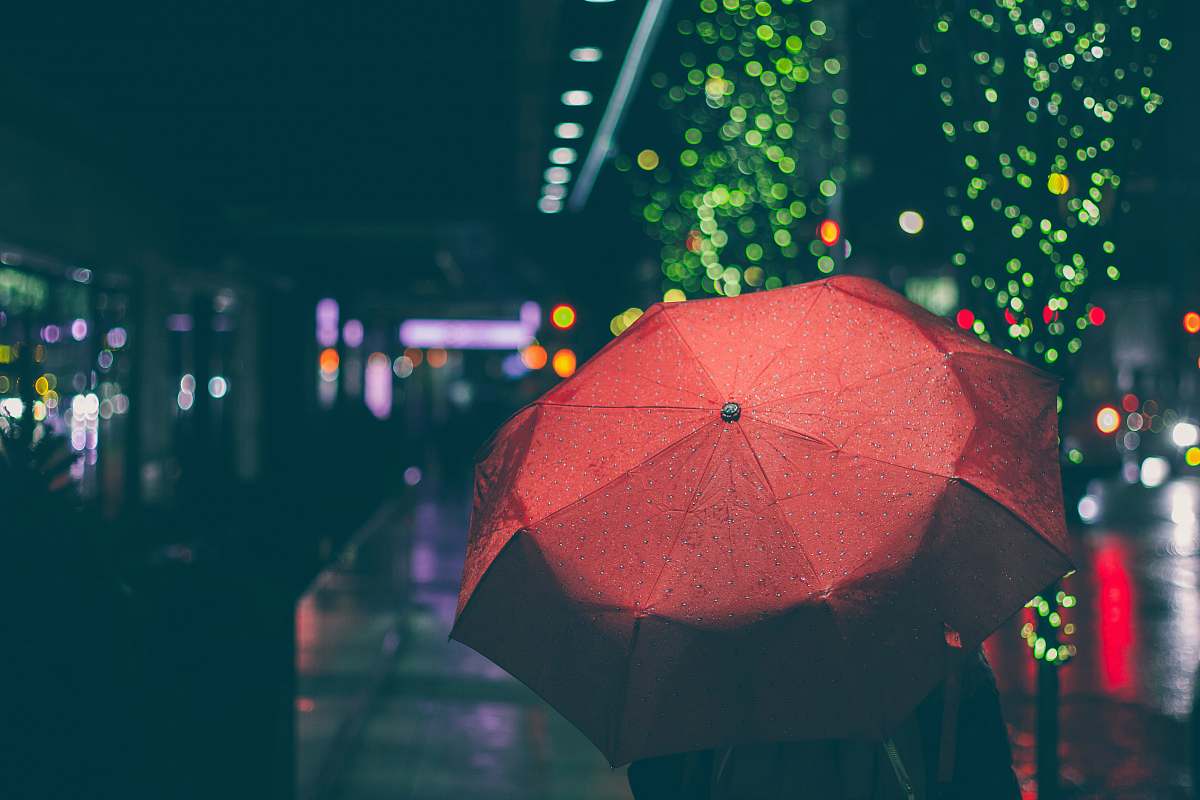 canopy person with red umbrella walking on street during nighttime rain