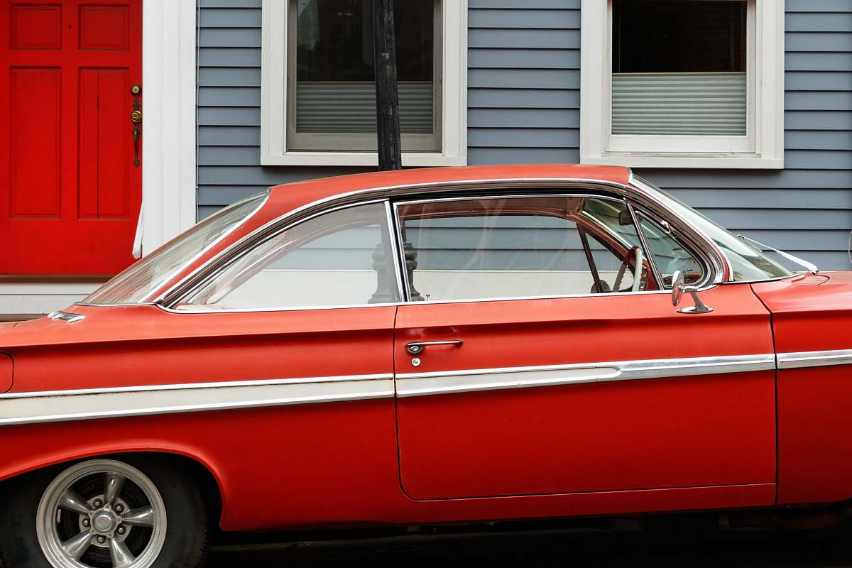 car classic red coupe parks beside gray and white wooden house automobile