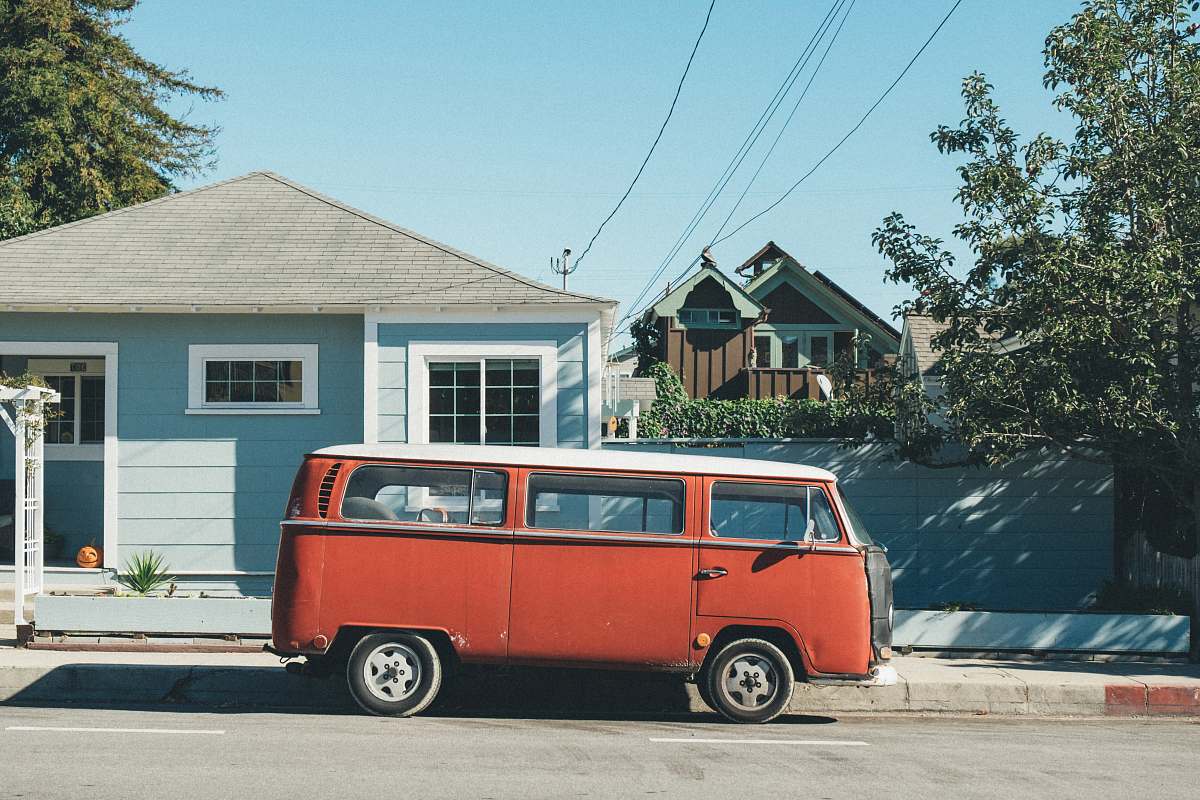 van red Volkswagen Samba parked in front of teal house caravan