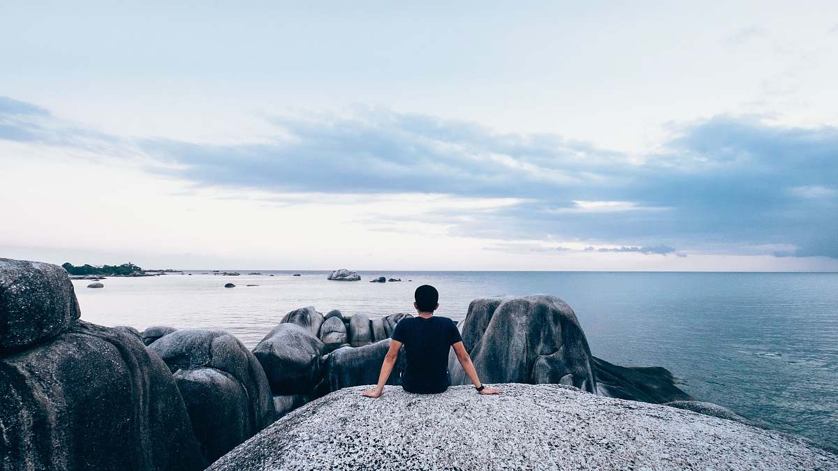 people man sitting on rock beside body of water sea