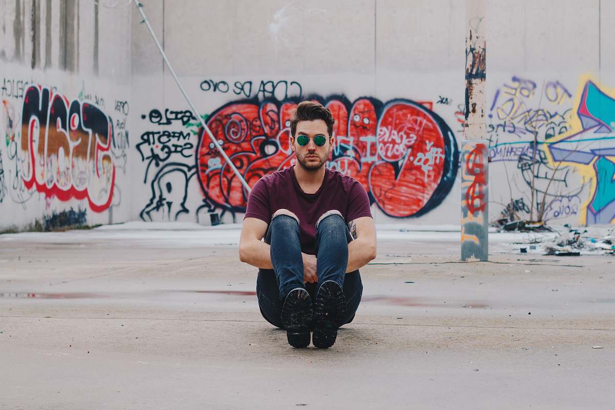 people man wearing purple shirt sitting in front of graffiti wall graffiti