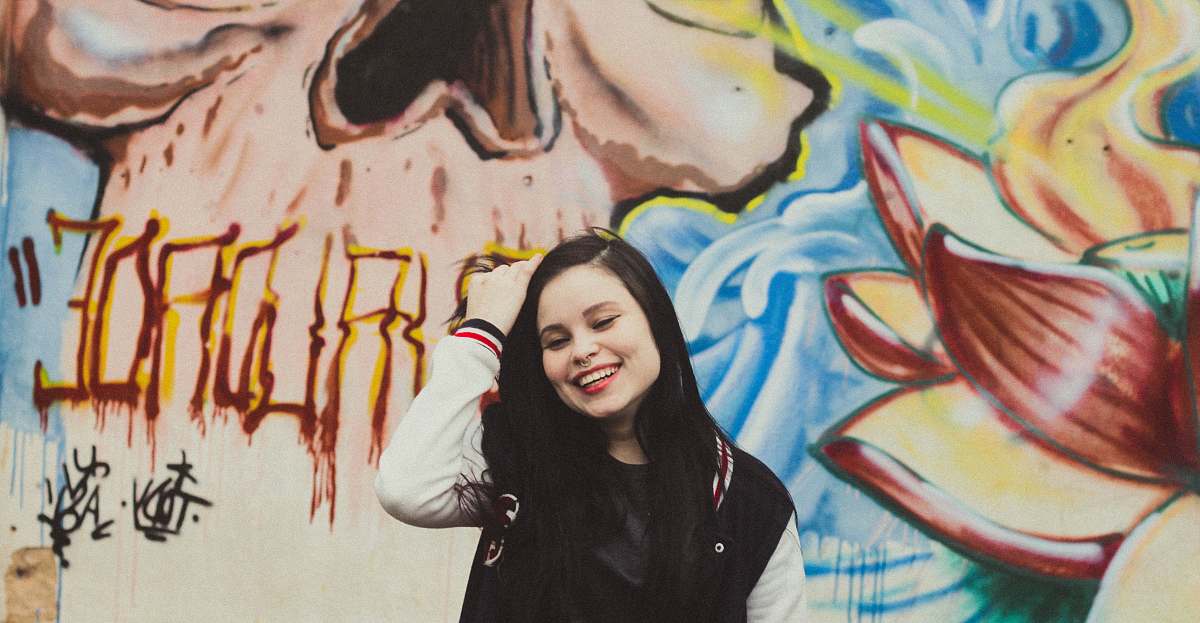 people woman wearing black and white letterman jacket standing in front of mural painting person