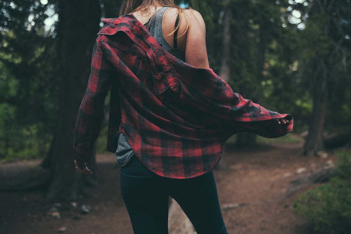 person back of person standing between tall trees human