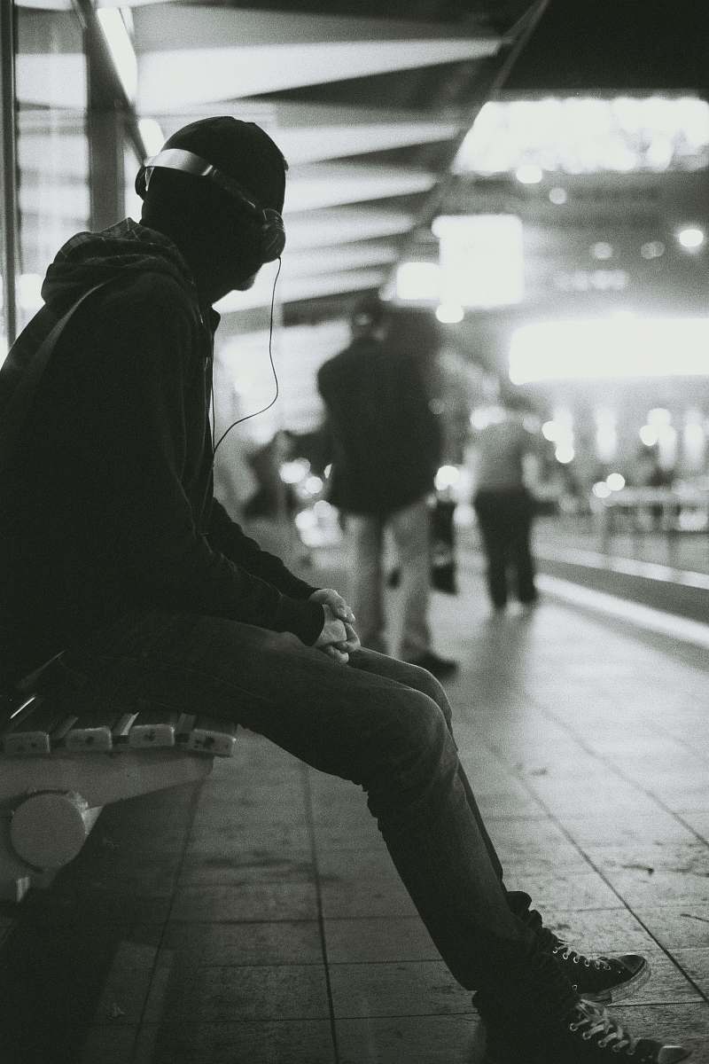 human grayscale photography of a man sitting on bench while listening music person