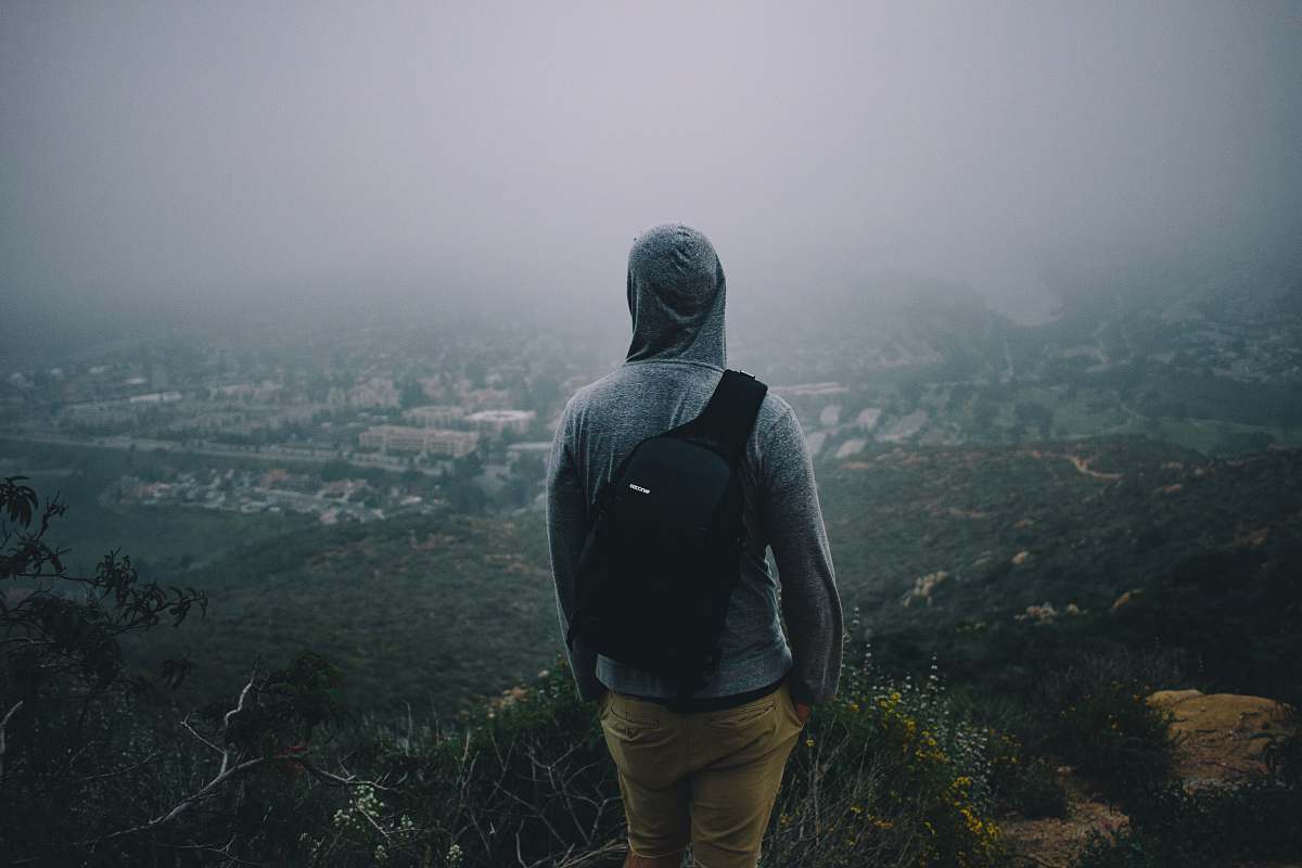 human man in gray hoodie with black backpack looking at the city from mountain peek person