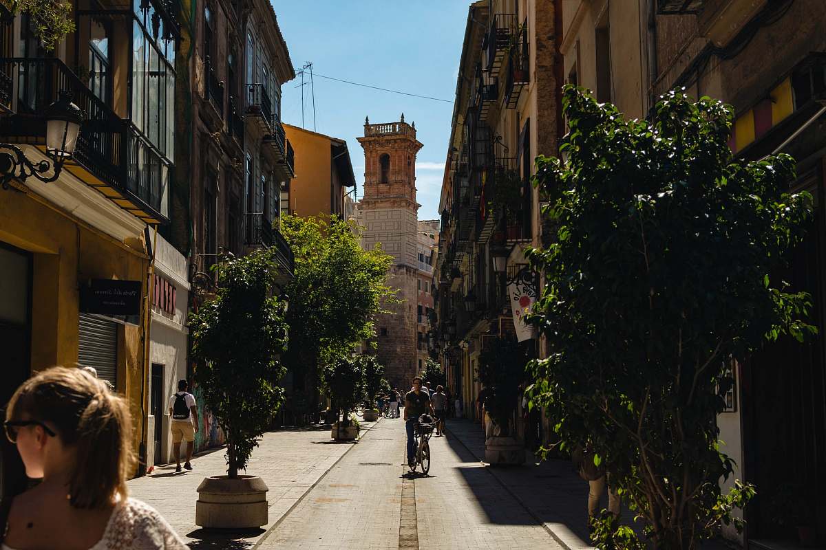 flora man riding bicycle near narrow street surrounded by buildings during daytime jar