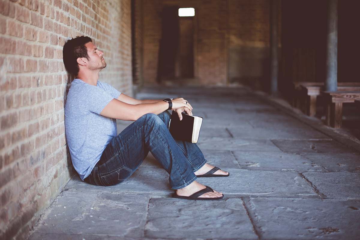 human man sitting on pathway holding book at nighttime person
