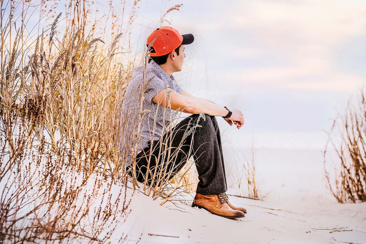 human man sitting on sand with wheat looking right during daytime person