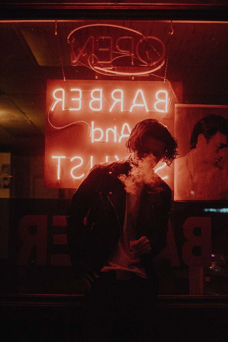 human man smoking in front of barber neon light signage person