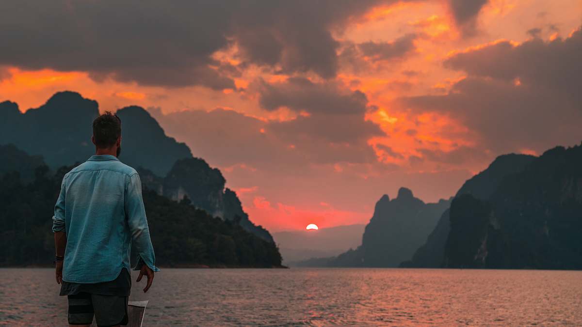 person man standing near edge facing body of water during sunset human