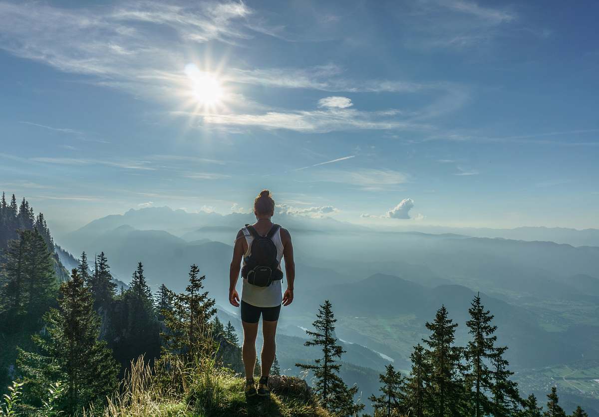 human man standing on green grass in front green trees field near mountains person