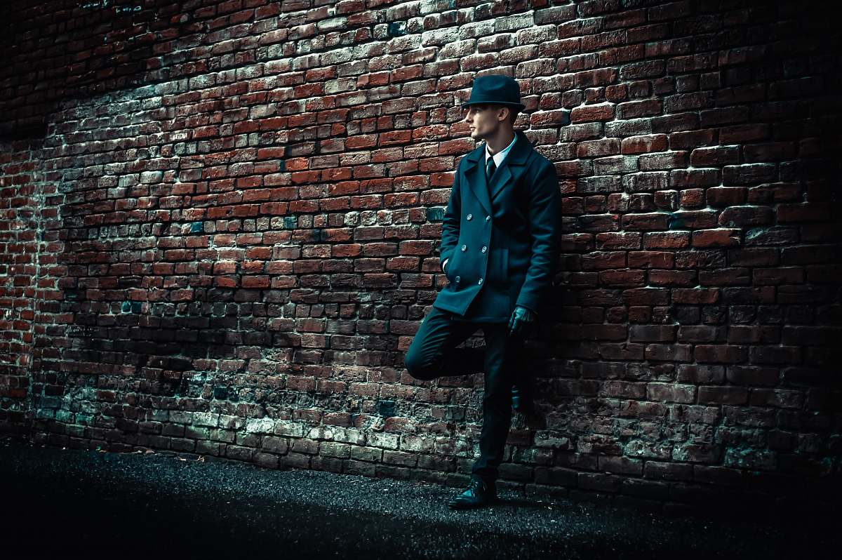 human man wearing black coat leaning on brown brick wall brick
