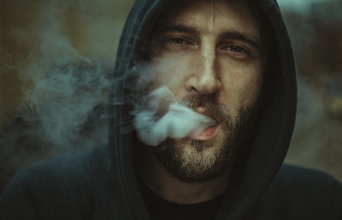 human man wearing black pullover hoodie blowing white smoke person