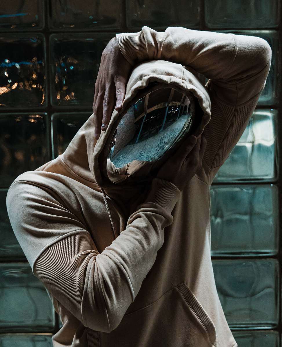 human person in chrome mask and pullover hoodie behind clear glass wall person