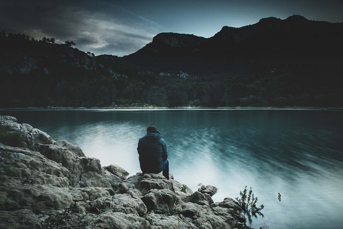 person person sitting on rock near body of water human