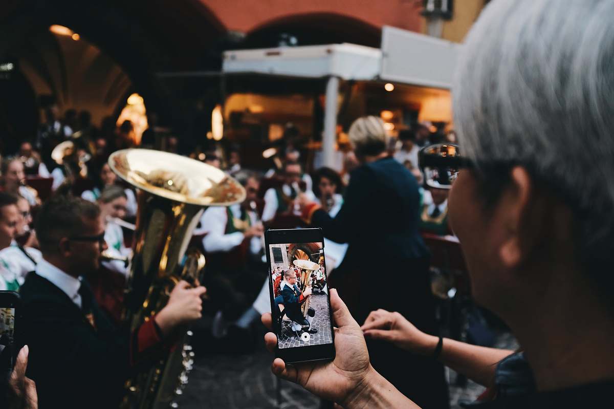 human selective focus photo of woman holding phone taking a photo of man playing instrument person