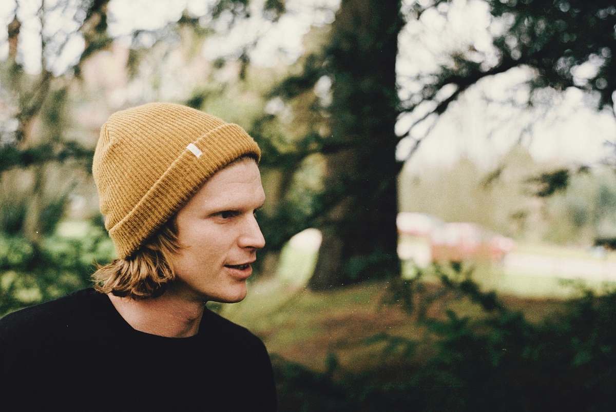 hat shadow depth of field photography of man in black shirt standing near trees beanie