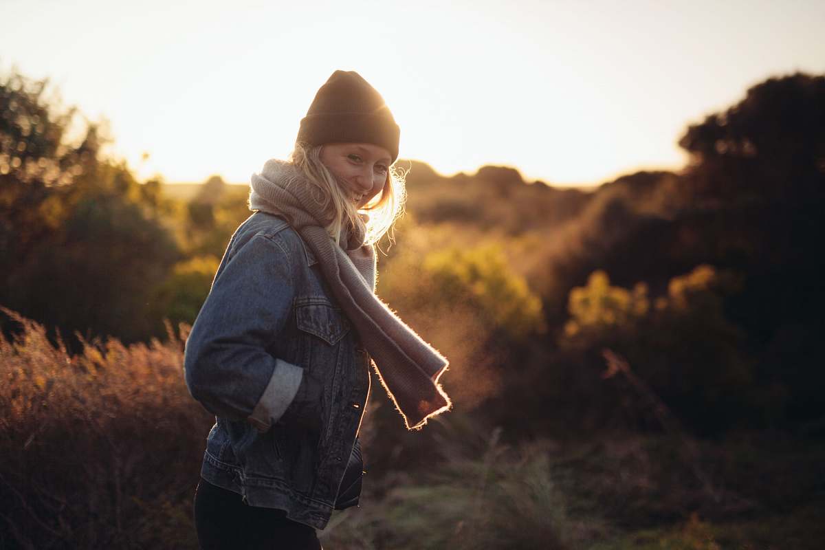 human smiling woman taking photo near trees and brown grass during sunrise person