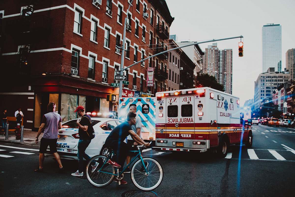 person three people walking near man riding bicycle on street near ambulance human